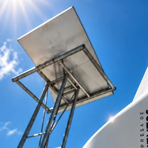 Antena Starlink vista de baixo, presa a um suporte metálico, com o sol e o céu azul ao fundo