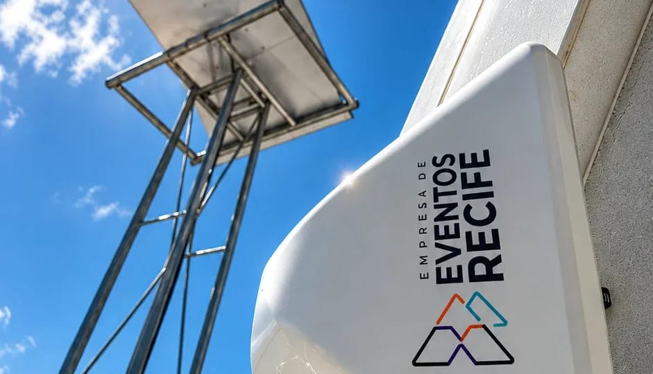 Suporte metálico da antena Starlink contra o céu azul, ao lado do modem 5G branco em primeiro plano